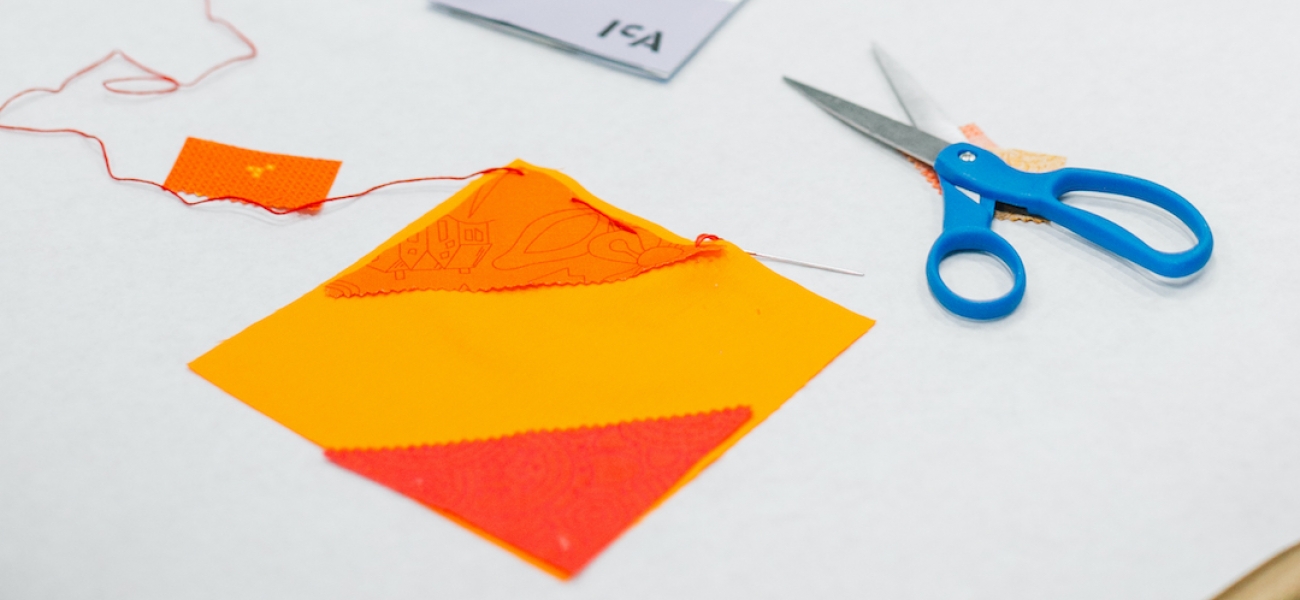 A piece of orange fabric square next to a pair of scissors on a table.