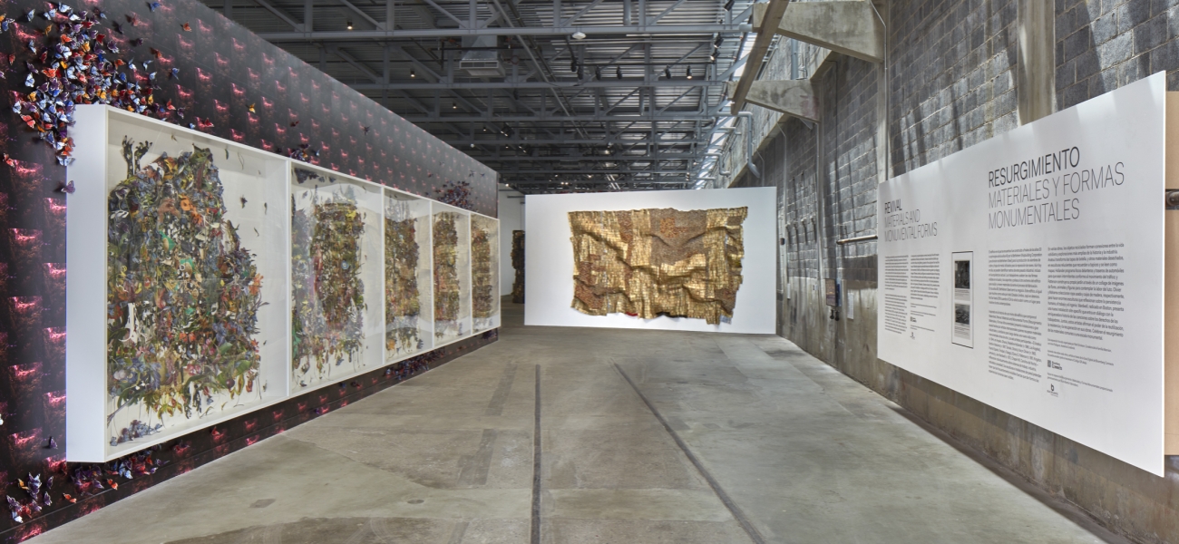 A golden metal tapestry hangs across from a purple wall with large panels and the gallery introduction text