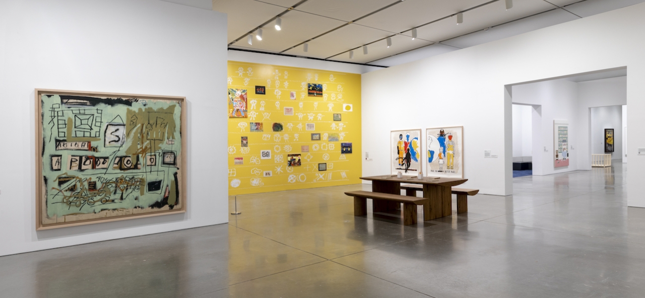 A gallery with a painting featuring childlike mark-making and mint green in the foreground and a bright yellow wall-sized work in the background. 