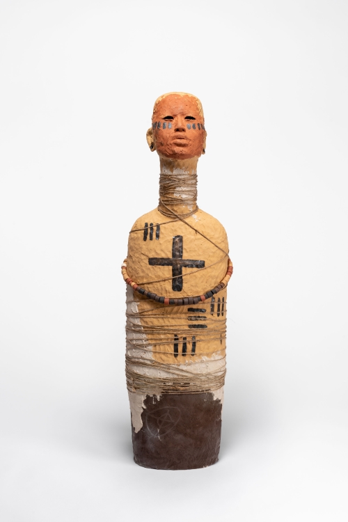 An elongated clay bust with cord and beads wrapped around it and black painted line markings