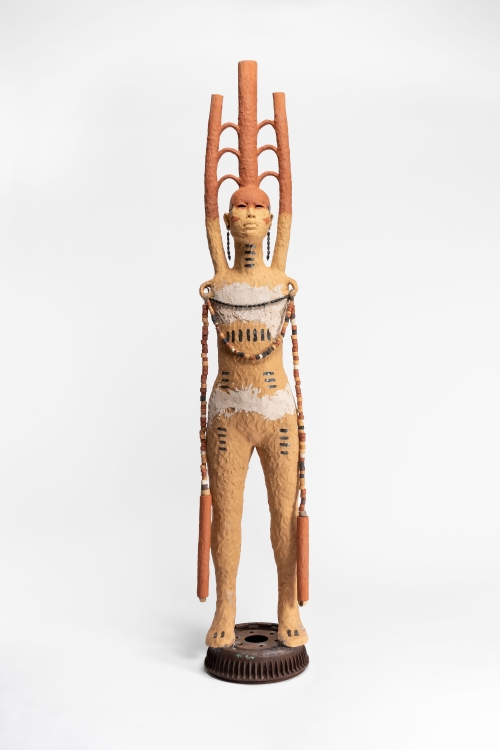 A tan armless clay figure with three connected pipes emerging from its head and shoulders