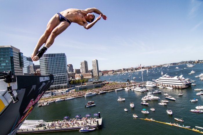 A man wearing a Speedo dives off a roof in the Seaport harbor