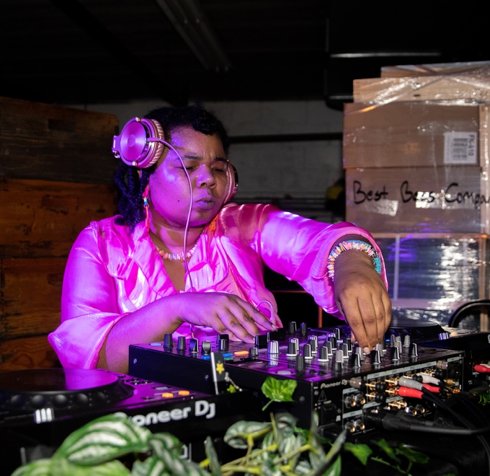 A DJ with pink headphones and blouse playing a set