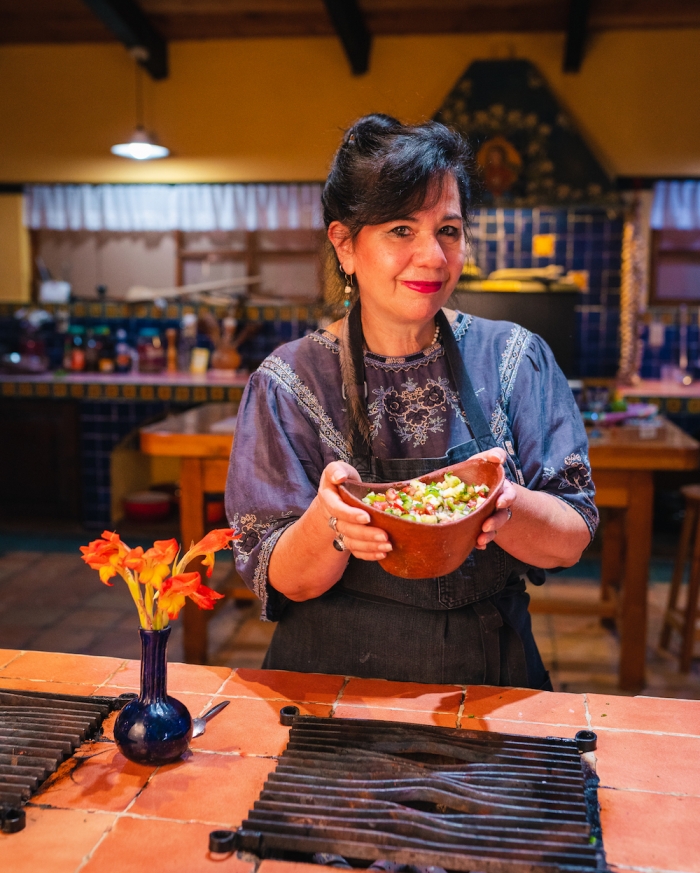 Chef Susana Trilling in a colorful kitchen holding a dish.