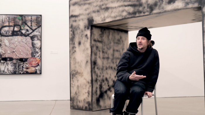 Man standing in front of sculpture with his hands gesturing as he speaks
