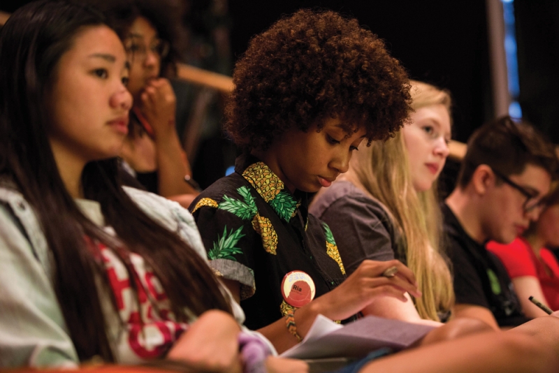 Teens taking notes while listening and sitting in an audience.