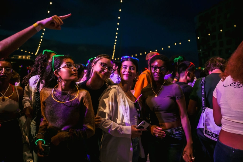 A group of teens smile for a photo amongst a dancing crowd outdoors