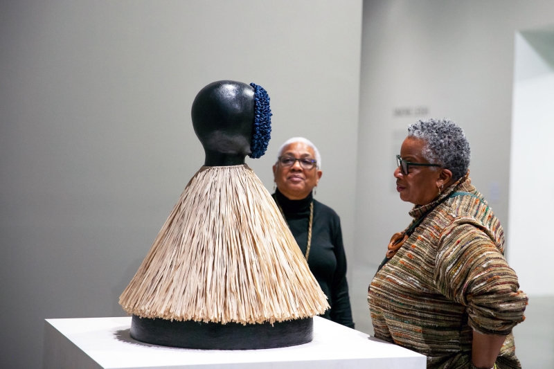 Two older Black women looking closely at a sculpture on a pedestal