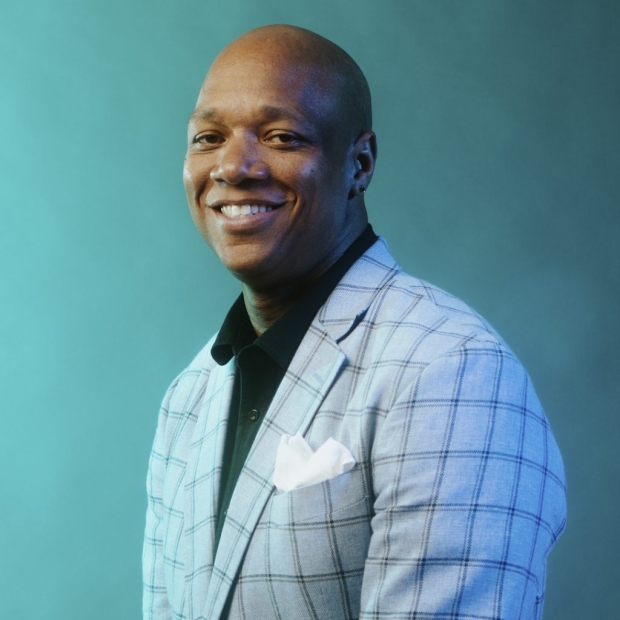 Headshot of a smiling Black man against a teal background