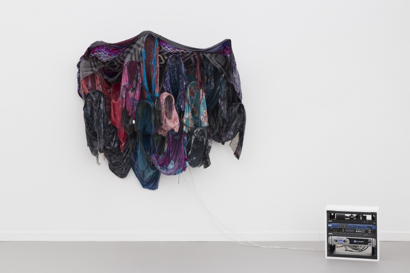 A sculpture mounted on the wall and composed of a cluster of colorful housedresses.