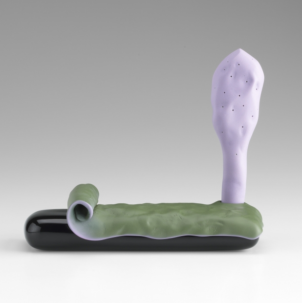 A small ceramic sculpture comprises a shiny black base partially covered by a curling thin green layer and, to the far right, a vertical light purple leaf-like structure.