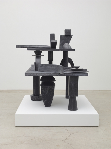 A sculpture of various ashy black, solid geometric stone and steel shapes stacked and balanced on top of one another.