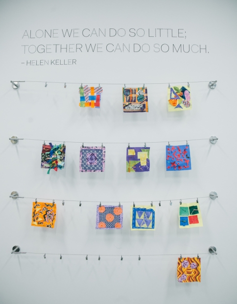 A wall with colorful artworks pinned on horizontal strings