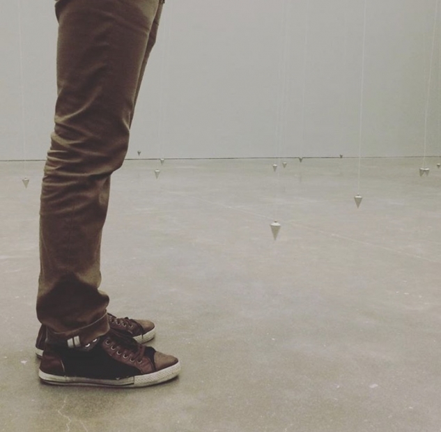 A pair of small legs standing amid a cement floor with swinging pendulums.