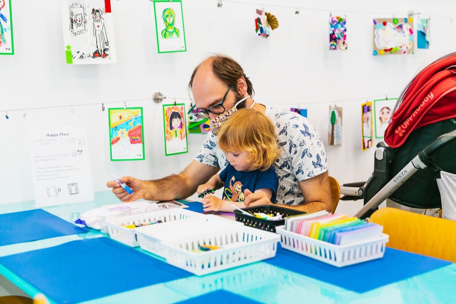 A parent and a young child work on creating art together at a table
