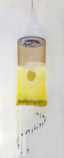 A form that looks like a mobile or a fishing net with orange and yellow fibers hangs suspended. The net hangs from a white disc with a hand-drawn, mermaidlike figure and the words "Rios vivos, pueblos libres" (living rivers, free people).