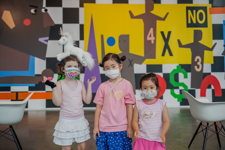 Three children wearing colorful masks stand in the ICA lobby.