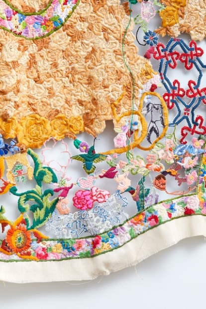 Close up of embroidered artwork featuring small flowers, birds, and other shapes