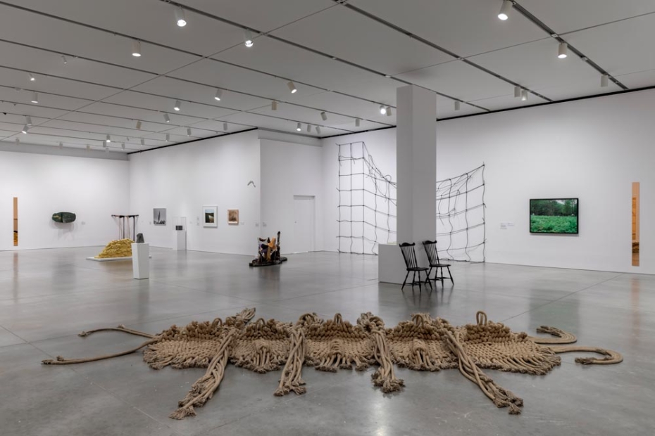 Wide gallery with works on walls and sculptural works, including large knit installation on floor