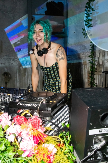 A DJ with green hair tied up laughs as they play a set