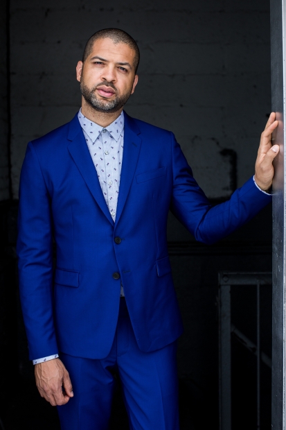 Portrait of Jason Moran from the Family Ball performance in a blue suit leaning against a wall with one hand.