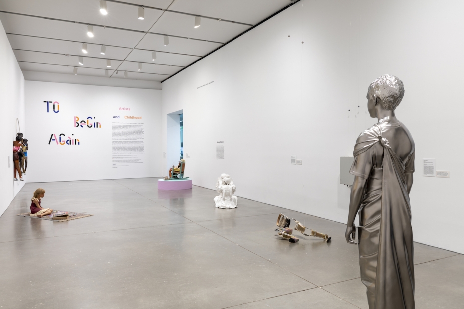 A gallery with several sculptures of children, including one in silver in the foreground, and the text "To Begin Again: Artists and Childhood" on the far wall.