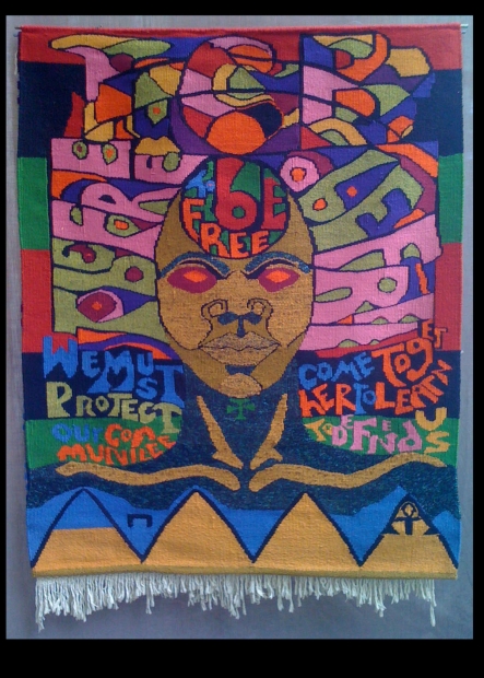 A colorful textile depicting a face with brown skin and red eyes surrounded by words including "To be free." 
