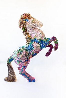 Sculpture of a horse rearing, encrusted with colorful beads, bells, sequins, and other homespun materials.