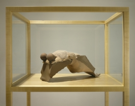 A sculpture of an abstracted torso and legs of a female figure arching in a display case.