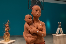 Closeup of a clay female figure holding a baby with other sculptures in view behind