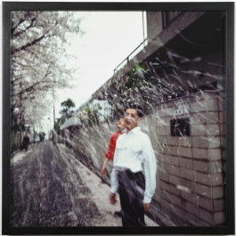 A square color photograph of two Asian youths standing on a street under a flurry of cherry blossoms.