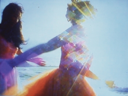 A color photograph reproduces two figures running in close-up over a brightly sunlit beach, the image abstracted by colorful solar flare.