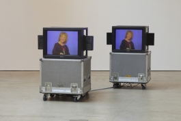 A sculpture of two cube monitors on flight cases with video stills of a light-skinned woman with blond hair holding a rose. 