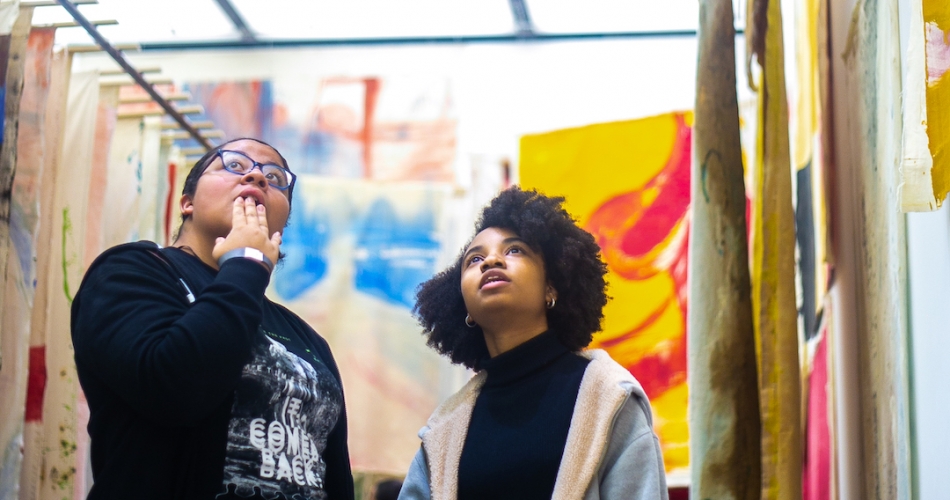 Two teens looking at the unstretched paintings hung in Vivian Suter's immersive installation.