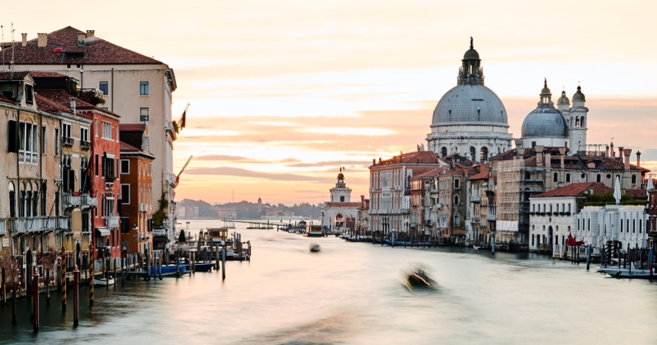 View of a Venetian canal at sunset with a row of buildings on the left and the Basilica of Santa Maria della Salute on the right