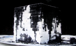 A video still of a stack of sugar cubes covered in dark oil on a silver plate.