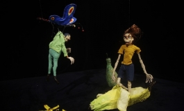A video still of crudely-rendered clay figures caught mid-action in a dark, ambiguous space.