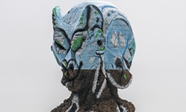 A bust by Huma Bhaba, that is gray and organic in texture, with the top covered in light blue paint. 