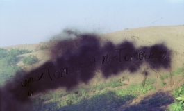A color photograph of a sandy dune with plants obscured by a cloudy, black form with the words "yes Tomorrow no Tomorrow" scratched into it. 