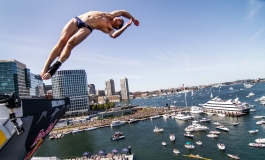 A man wearing a Speedo dives off a roof in the Seaport harbor
