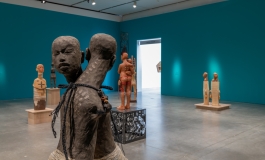Two interlocked grey figures in front of other clay figures in view in blue gallery