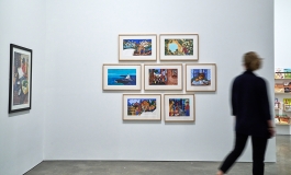 Person walking by a grouping of colorful framed works on the wall