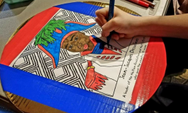 A hand holding a marker coloring in a portrait of Jean-Jacques Dessalines, an African-American figure wearing an 18th-century French-style army uniform.