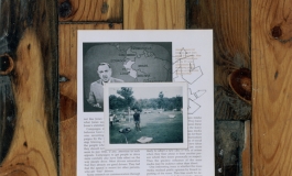 A color photograph depicts a snapshot of a Black man standing in a yard lying, on top of a page from a textbook showing a photo of Walter Cronkite next to a map of South America, displayed flat on a wooden floor.