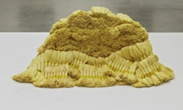 A sculpture made of bundles of yellow-colored linen and wool thread piled on a large white platform.