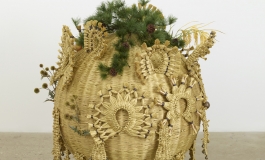 A spherical sculpture made of golden artificial straw and decorated with straw ornaments and artificial plants.