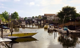 A color photograph of a waterway with many boats and a bridge connecting two shores dotted with houses and trees.