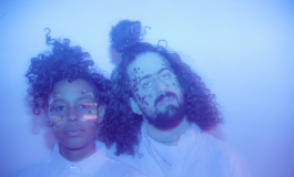 The two members of Optic Bloom with stars on their faces in a blue colored photograph. 