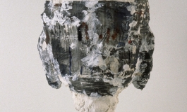 A sculpture of an abstracted, figurative head comprised of mixed materials and suspended upright on a display plinth.