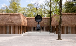Building covered with straw thatched roofing and a large black sculpture standing on a plinth in front of it